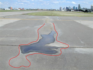 Photo showing a low-severity depression with standing water in it. A red line has been drawn on the photo to outline the area with the depression.