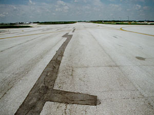 Overview of a long, narrow, wandering patch at the centerline of a taxiway pavement. There is noticeable cracking within the patch area.