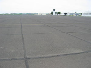 Overview photo of an apron pavement with a uniform rectangular pattern of low-severity transverse and longitudinal cracks. The pattern is the result of cracks that have reflected through the asphalt surface at the joints of the PCC slabs below.