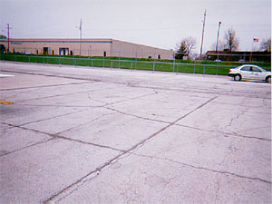 Overview photo of an apron pavement with a uniform rectangular pattern of medium-severity transverse and longitudinal cracks. The pattern is the result of cracks that have reflected through the asphalt surface at the joints of the PCC slabs below. Some spalling is visible at the cracks.