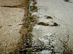 Close-up photo showing a longitudinal joint between a PCC and an asphalt pavement. The asphalt surface in the photo has a considerable amount of distress that has occurred from shoving.