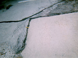 Overview photo showing an asphalt surface around the corner of a PCC slab. The asphalt at the joint between the PCC and asphalt surfaces is noticeably higher than the PCC slab.
