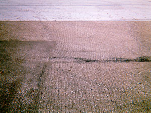 Overview photo showing some signs of slippage cracking, but no visible cracks yet. In the photo, cut grooves in the pavement surface have noticeably warped due to turning wheels or braking.