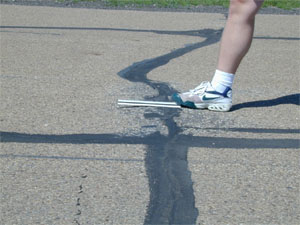 Close-up photo of a transverse joint with a slight but visible swell in the pavement surface at the joint. A ruler has been placed across the joint in the longitudinal direction to show that there is an upward bulge in the pavement at the joint.