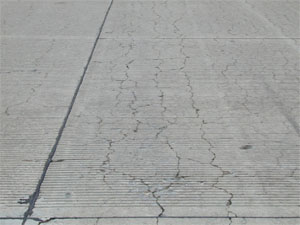 Overview photo of a PCC slab with a noticeable pattern of fine cracks spread over the entire surface area of the slab. Some of the cracks are spalled.