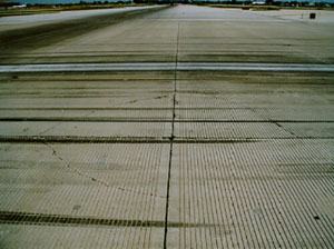 Overview photo showing a corner where four PCC slabs come together. Three of the four slabs in the photo have low-severity corner breaks. Each corner break is a fairly tight, single, non-spalled crack.