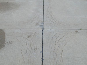 Close-up photo showing a corner where four PCC slabs come together. All four slab corners in the photo show a series of crescent-shaped D-cracks. The cracks are all tight with no visible spalling.