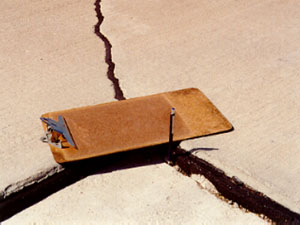 Close-up photo showing a transverse joint with a 1 1/2 in (38 mm) difference in elevation across the joint. A clipboard is placed across the joint in the photo to illustrate that there is a height differential between the two slabs.