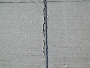 Close-up photo of a transverse joint with low-severity joint seal damage.  The silicone sealant in the photo is in good condition, but it is noticeably debonded from one side of the joint.