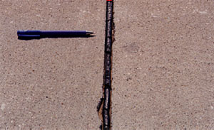 Close-up photo of a transverse joint with medium-severity joint seal damage.  The asphalt sealant in the photo is not in good condition, and noticeably debonded from the sides of the joint.