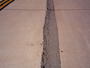 Overview photo of a longitudinal joint with a long narrow asphalt patch along the joint. The patch is showing visible signs of distress, with spalling and secondary cracking along one side of the patch.