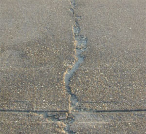 Close-up photo of a single high-severity crack in a PCC slab. The crack appears to be greater than 1 in (25 mm) wide and shows areas of spalling with high FOD potential.