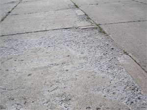Overview photo showing showing high-severity scaling. The PCC pavement surface in this photo is severely scaled, and there is noticeable loose material on the surface.