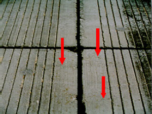 Close-up photo showing multiple small hairline shrinkage cracks on the pavement surface. Three red arrows are drawn on the photo to point to the location of the visible shrinkage cracks.