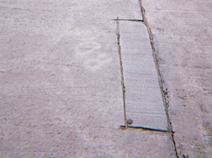 Overview photo of a transverse joint with a small rectangular PCC patch along the joint on one of the slabs. The patch is in very good condition with no visible signs of distress.
