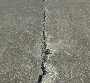 Close-up photo of a single medium-severity crack in a PCC slab. The crack appears to be 1/2 in (13 mm) wide and shows areas of spalling.