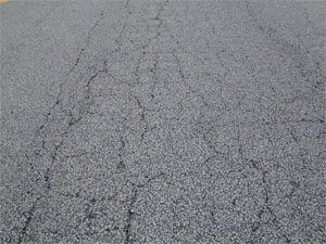 Photo showing a pattern of primarily light alligator cracking where                 some cracks are lightly spalled.  A few medium severity alligator cracks are visible in the pattern, but all all pieces are securely held in place.
